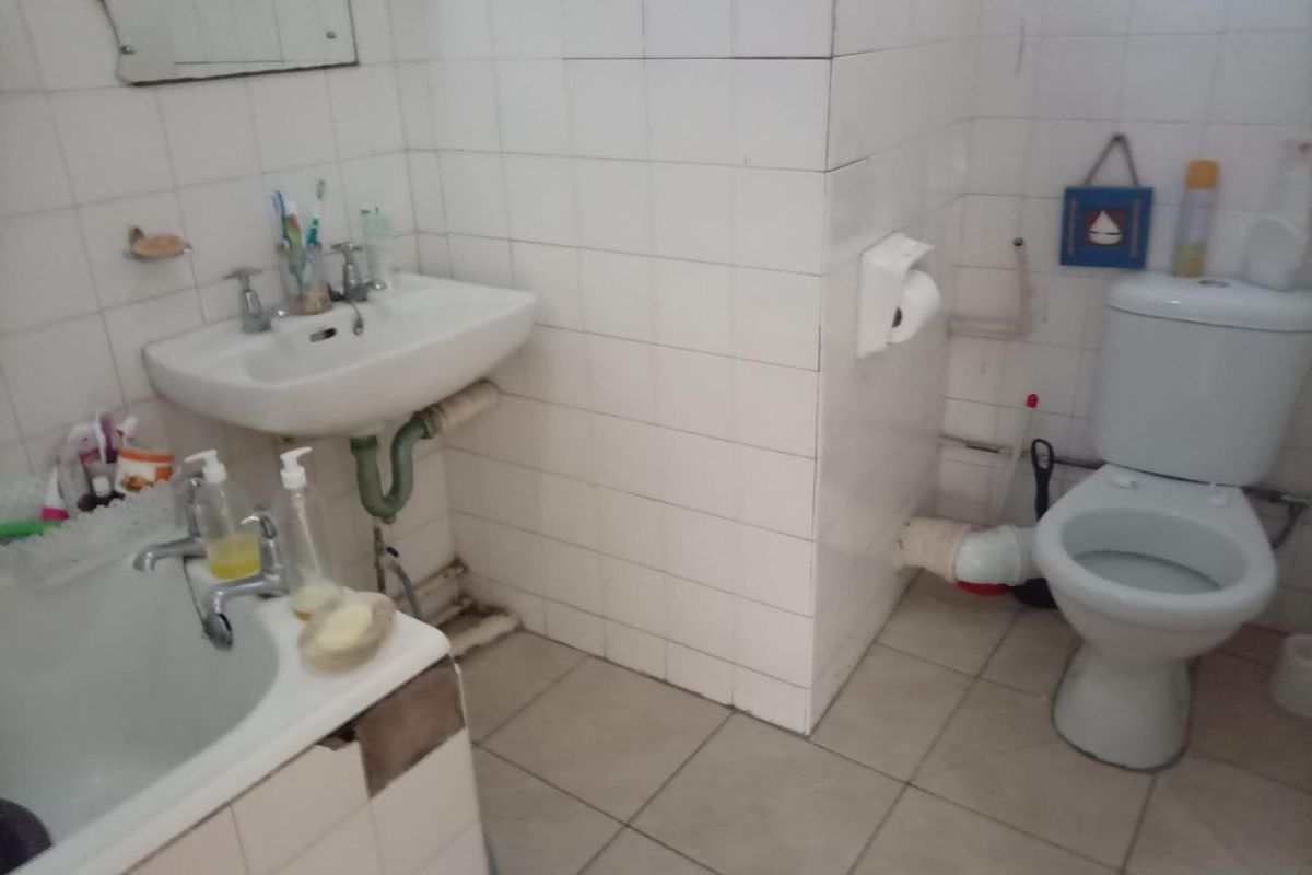 A dated bathroom featuring a pedestal basin, toilet, and tiled finishes, currently showing signs of wear and exposed plumbing.