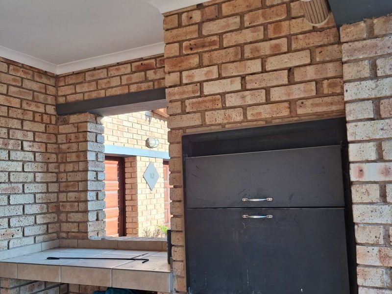 Covered patio area featuring exposed brick walls and a built-in braai with a tiled prep surface, ideal for outdoor entertaining.