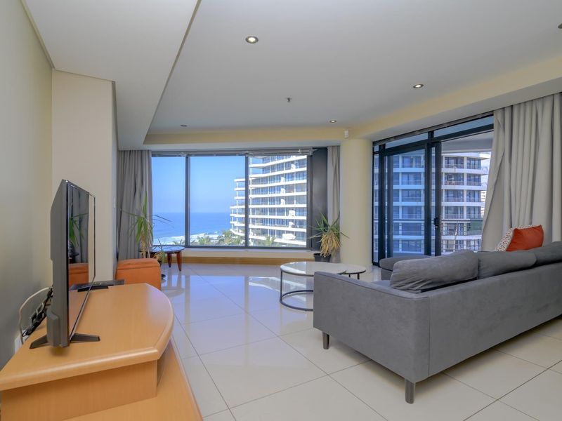 Spacious living area featuring large floor-to-ceiling windows, tiled flooring, recessed lighting, and direct access to a balcony with coastal views.
