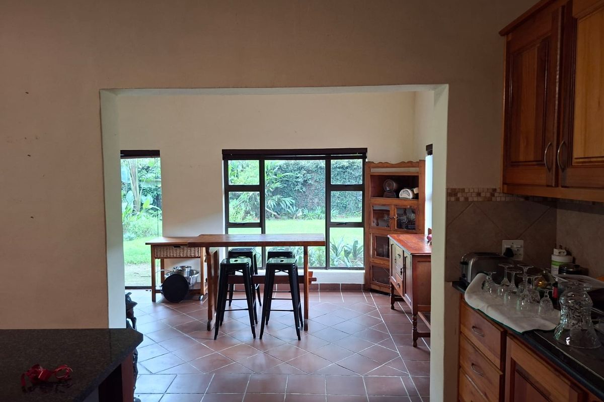 Open plan kitchen and dining area featuring wooden cabinetry, granite countertops, and large windows overlooking the garden.