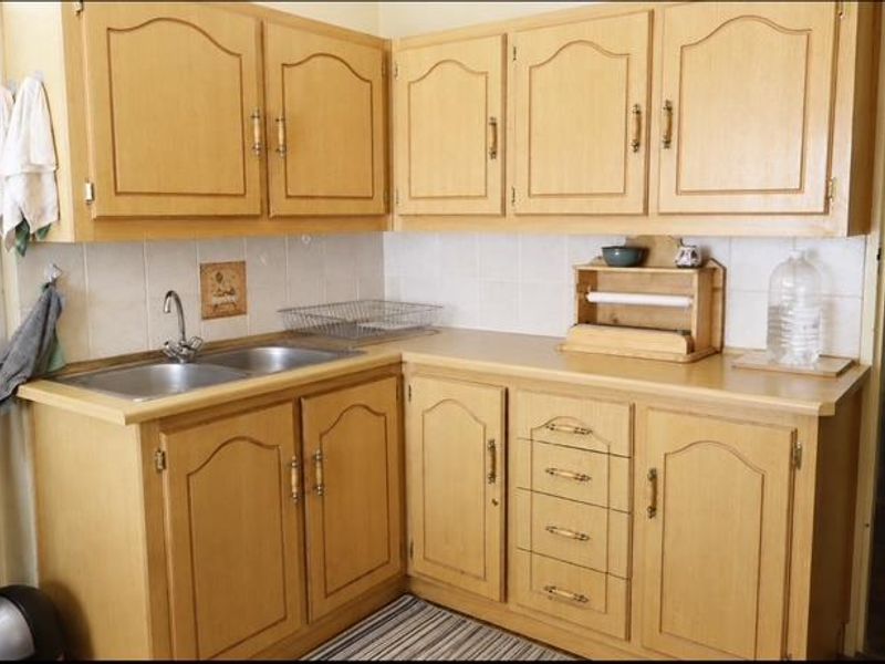 A functional kitchen featuring light wood-tone cabinetry, laminate countertops, a double stainless steel sink, and a tiled backsplash.