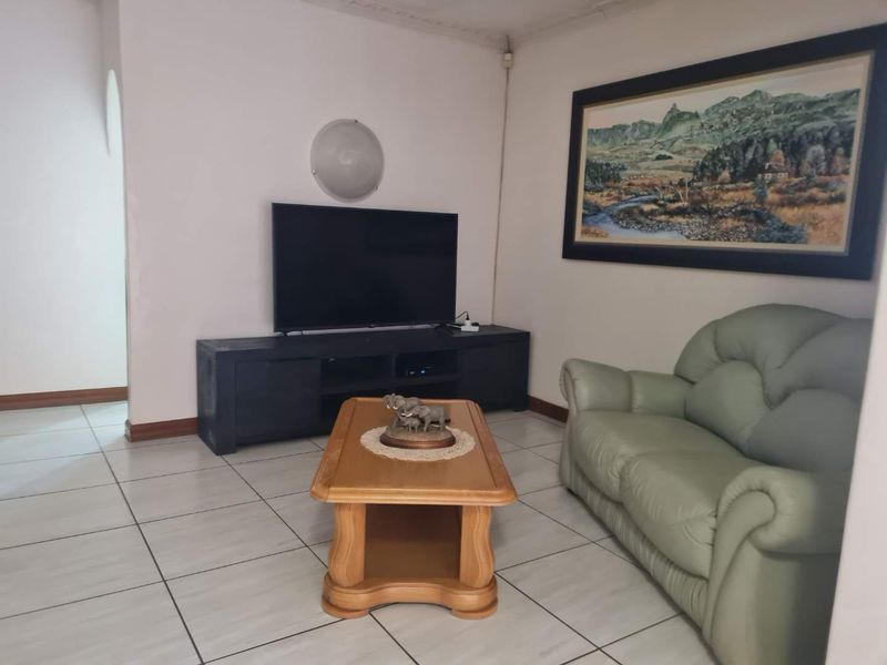 A living room featuring tiled flooring and decorative ceiling cornicing, providing a functional and neutral space for relaxation.