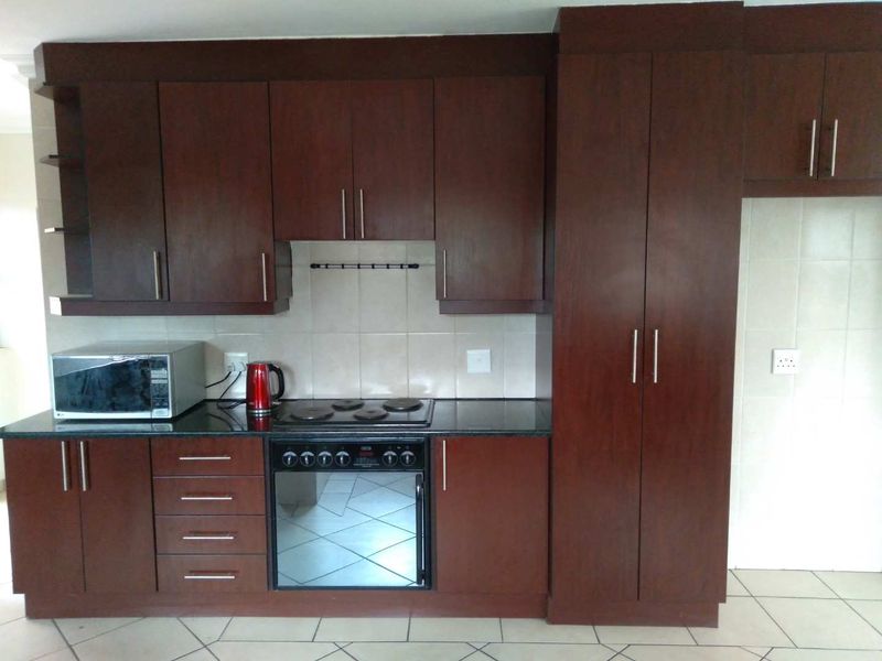 A functional kitchen featuring dark wood cabinetry, granite countertops, a built-in oven, electric hob, and tiled flooring.
