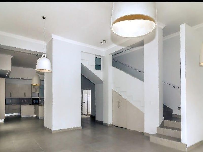 Spacious open-plan living area featuring tiled floors, a central staircase with under-stair storage, and a modern kitchen visible in the background.