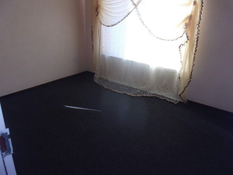 An empty bedroom featuring dark carpeting and a window with decorative curtains.