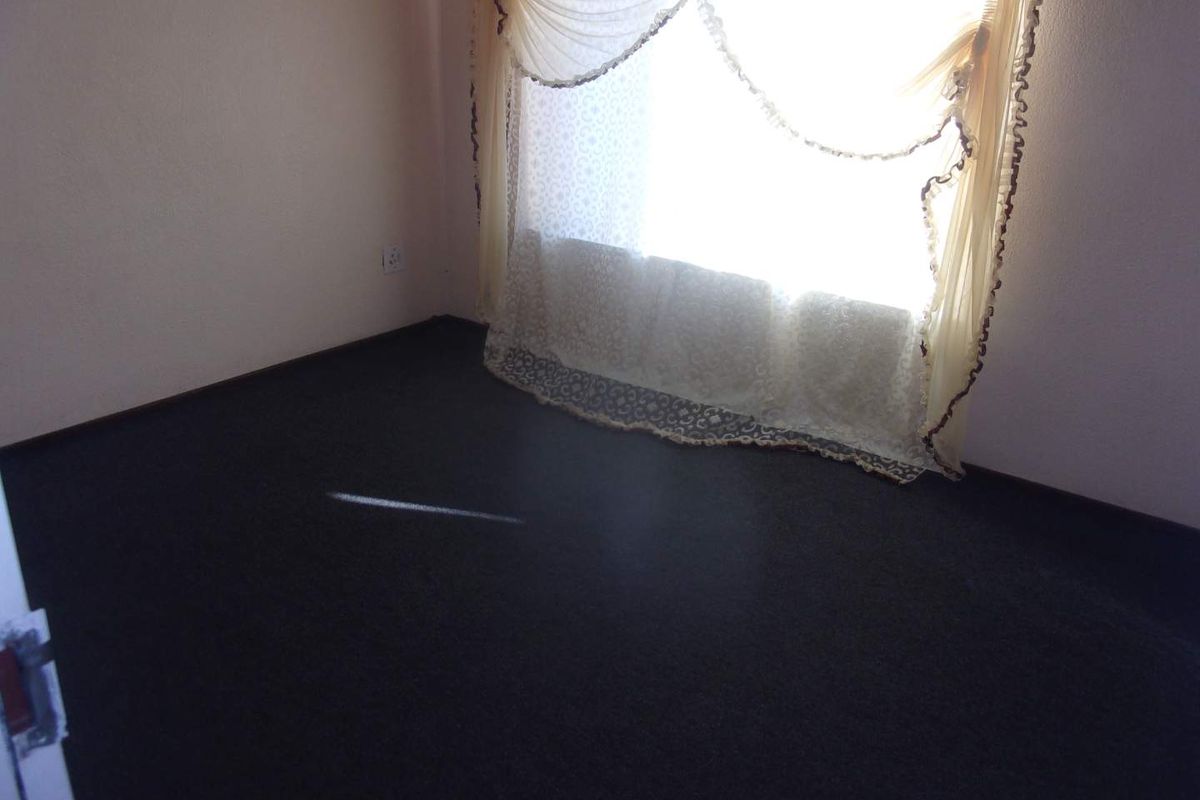 An empty bedroom featuring dark carpeting and a window with decorative curtains.