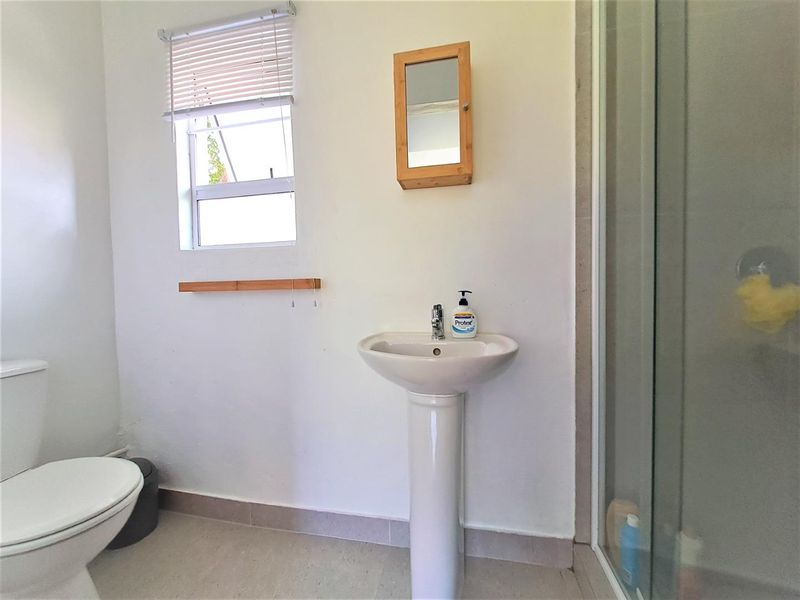 A functional bathroom featuring a pedestal basin, a shower enclosure with glass doors, and a toilet, finished with tiled flooring.