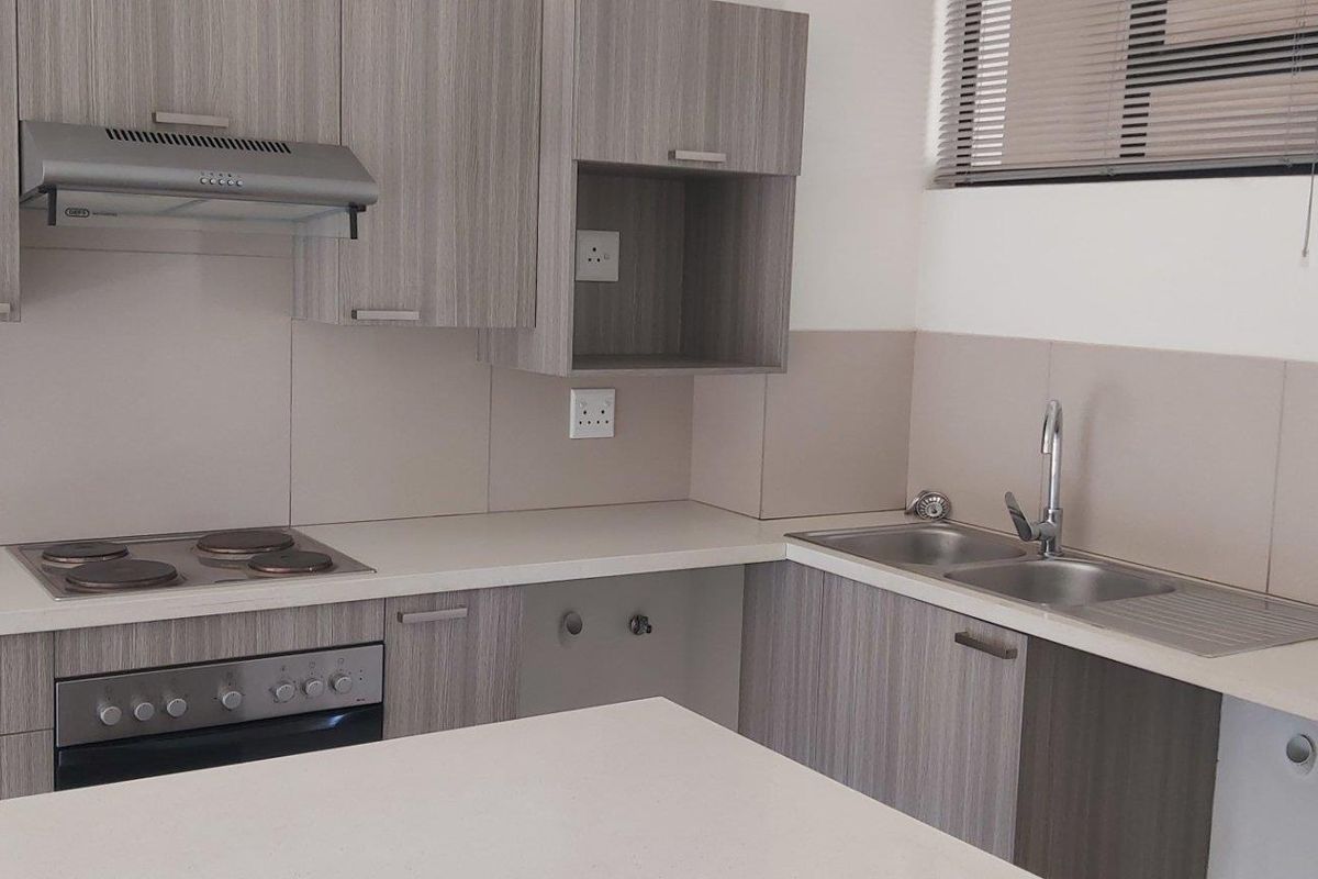 Modern kitchen featuring light wood-grain cabinetry, stone-look countertops, integrated electric hob and oven, stainless steel sink, and neutral tiled splashbacks.