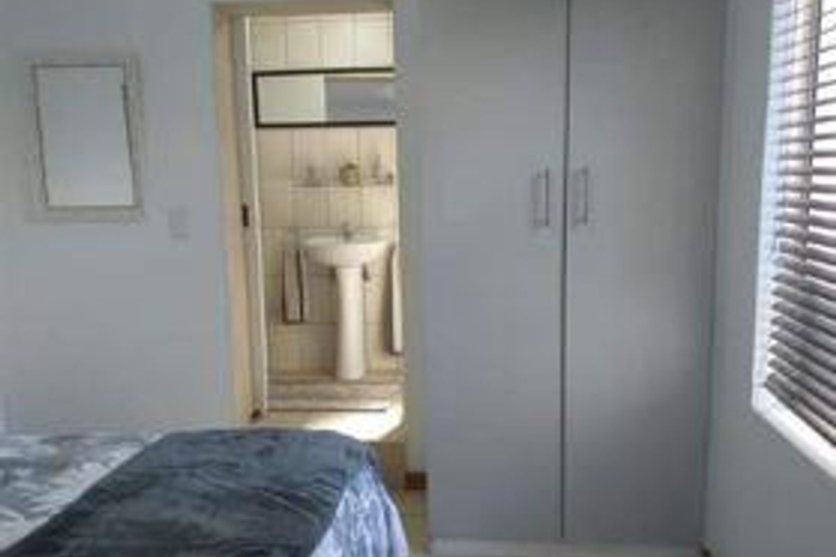 Bedroom featuring built-in cupboards and an en-suite bathroom with a pedestal basin and tiled finishes.