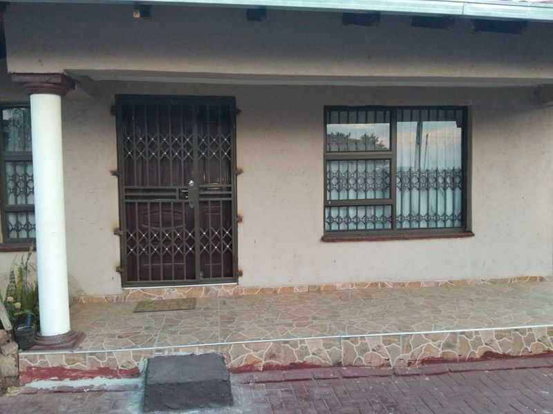 Front entrance area featuring a tiled porch, security gate, and security bars on windows, with a concrete column supporting the roof overhang.