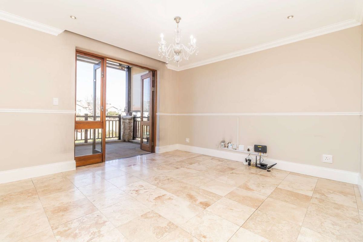 Spacious living area featuring travertine flooring, crown molding, and timber-framed glass doors opening onto a private balcony.