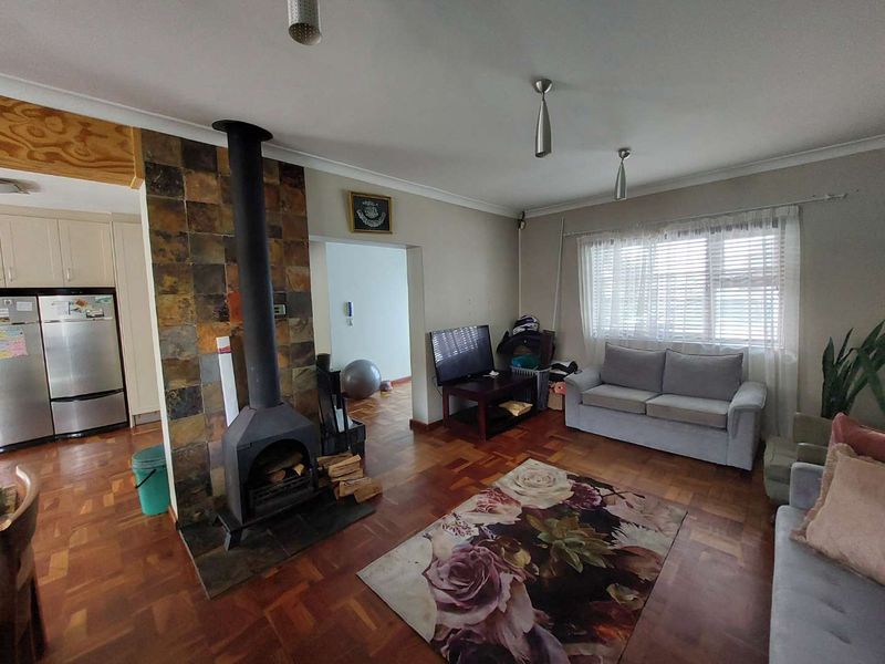 Open plan living area featuring a prominent slate-tiled fireplace, classic parquet flooring, and natural light through venetian blinds.