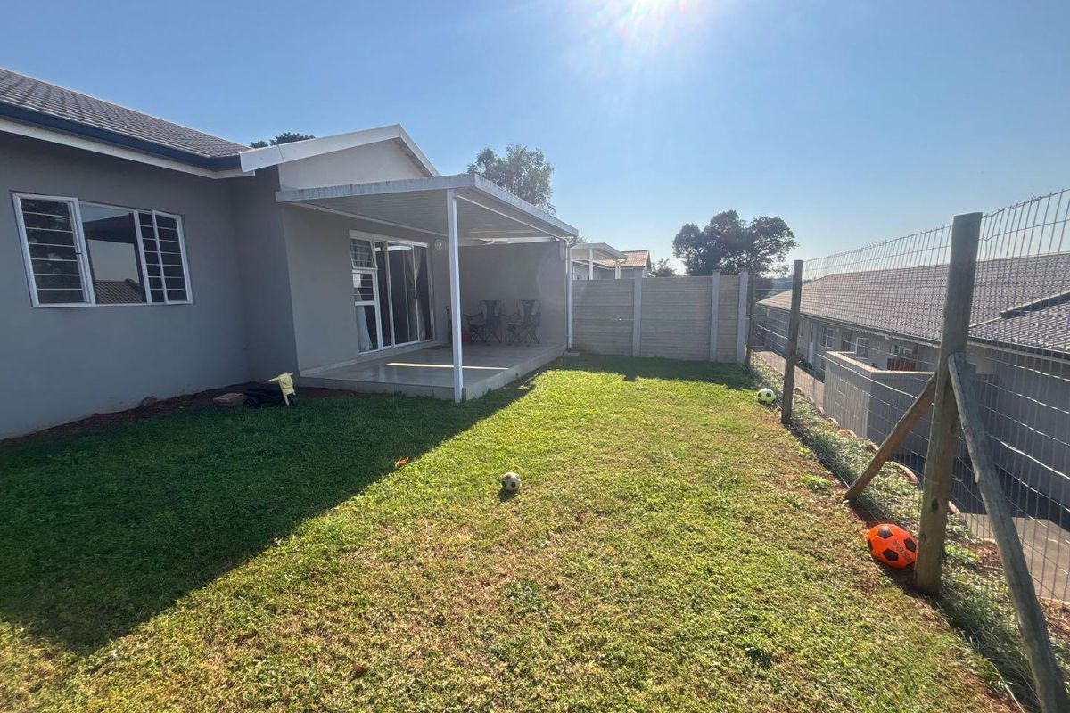 Rear view of the townhouse featuring a covered patio, sliding door access, and a private grassed garden enclosed by boundary walls and fencing.