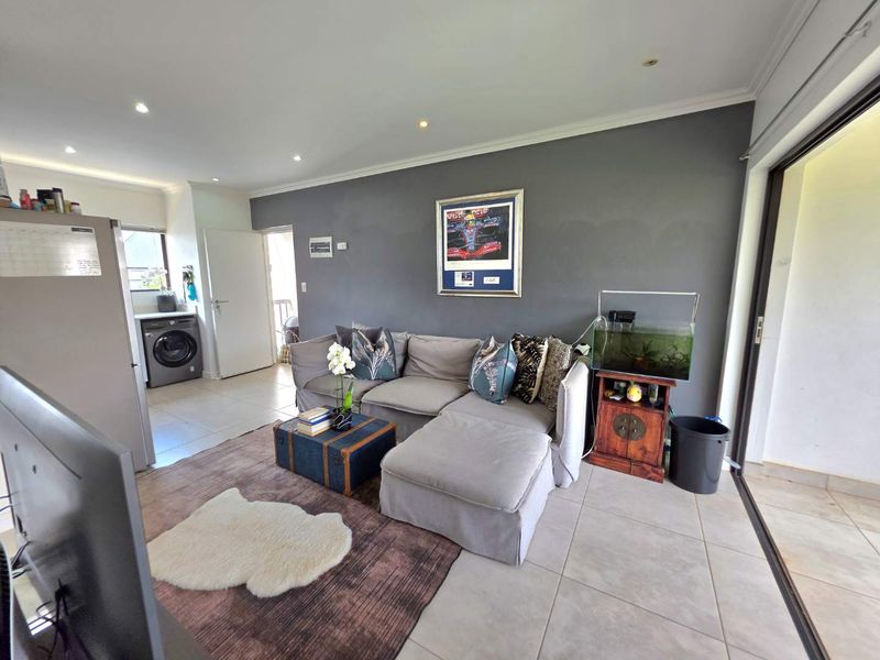 Open-plan living area featuring tiled flooring, recessed downlights, and a seamless transition to an outdoor space, with an integrated laundry nook.
