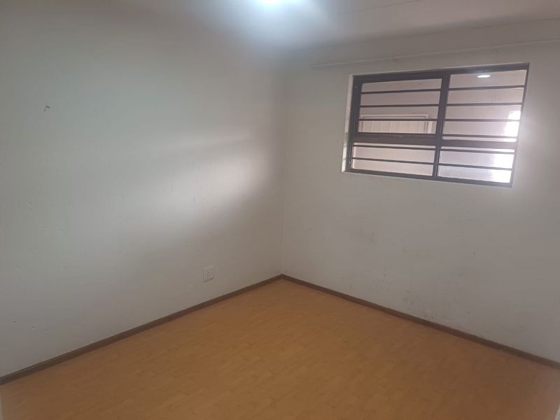 An empty bedroom featuring laminate flooring and a window fitted with security bars, requiring minor cosmetic updates to the wall finishes.