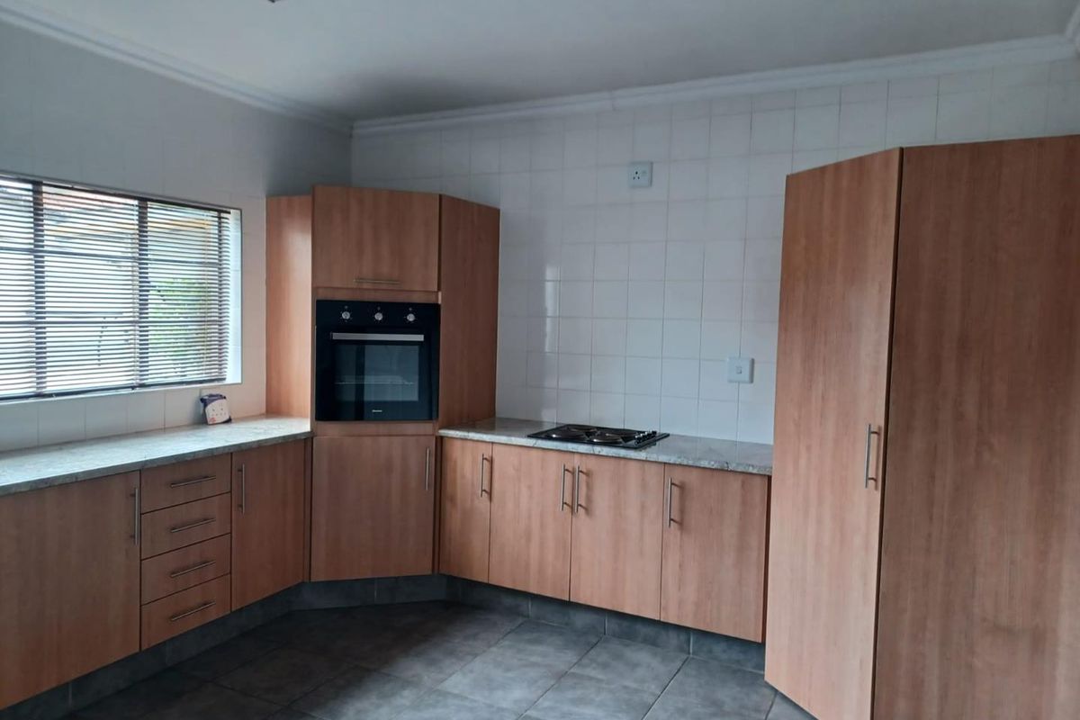 A functional kitchen featuring wood-look cabinetry, stone-effect countertops, a built-in oven, a gas hob, and tiled flooring.