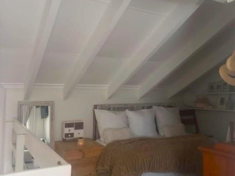 A cozy loft-style bedroom featuring exposed rafters, a sloped ceiling, and built-in shelving, creating a unique and intimate sleeping space.