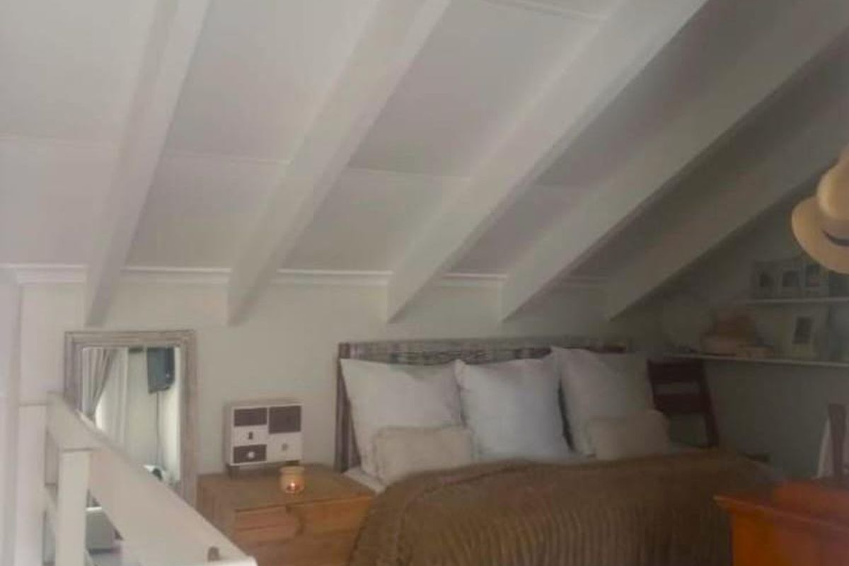 A cozy loft-style bedroom featuring exposed rafters, a sloped ceiling, and built-in shelving, creating a unique and intimate sleeping space.