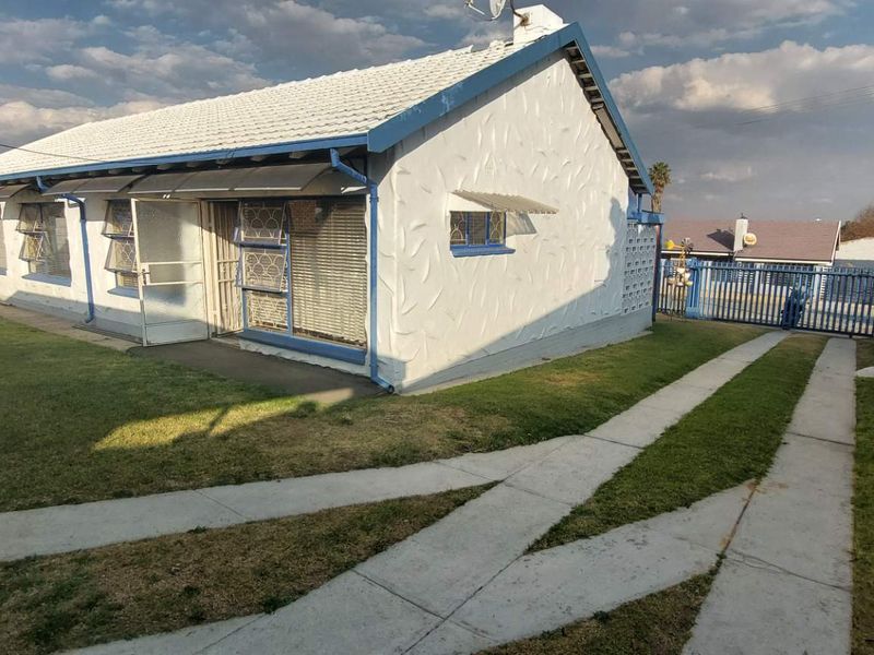 Front view of a single-story house featuring a tiled roof, security bars, and a concrete driveway within a fenced perimeter.