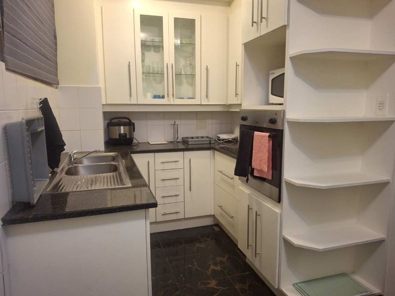 Compact kitchen featuring white cabinetry, granite countertops, a stainless steel double sink, and a built-in oven with integrated shelving.