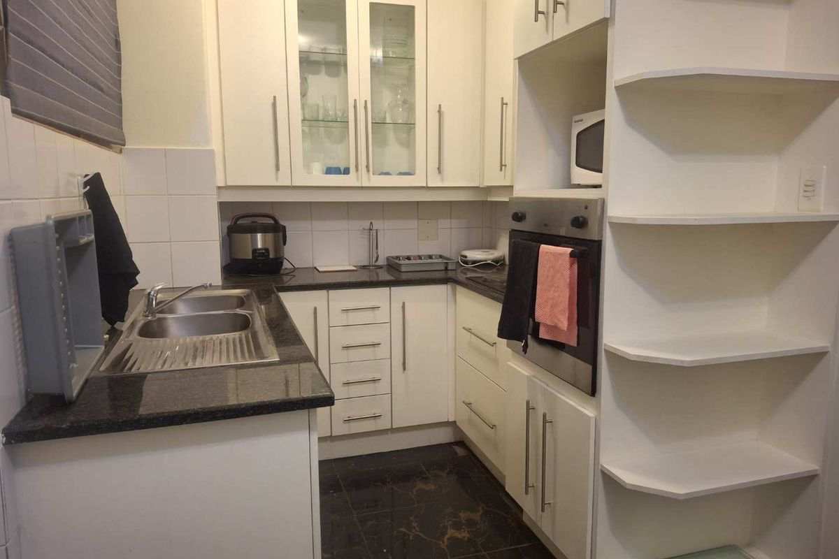 Compact kitchen featuring white cabinetry, granite countertops, a stainless steel double sink, and a built-in oven with integrated shelving.