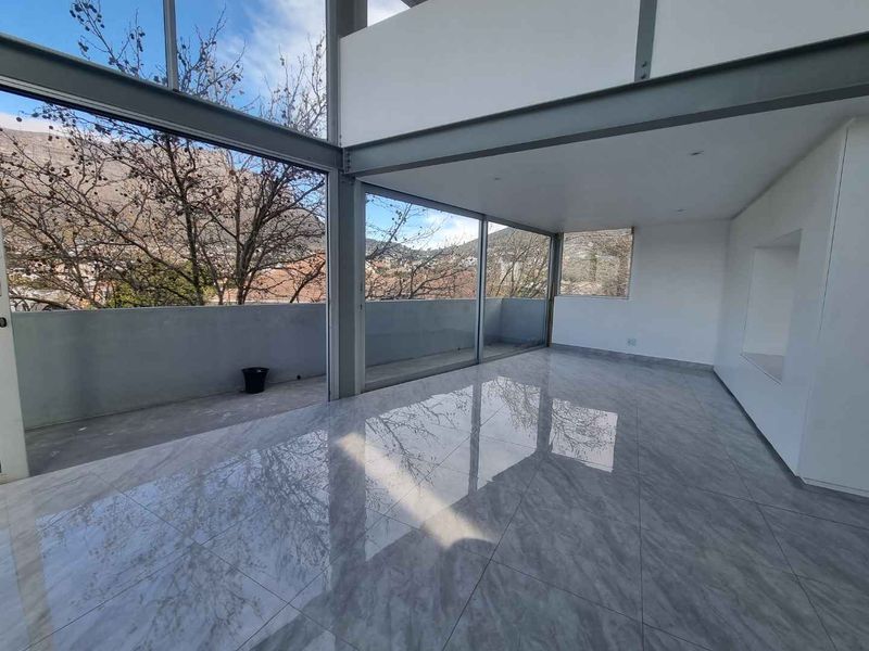 Spacious, modern open-plan living area featuring polished porcelain tiles, exposed steel structural elements, and expansive floor-to-ceiling glass doors opening onto a private balcony.