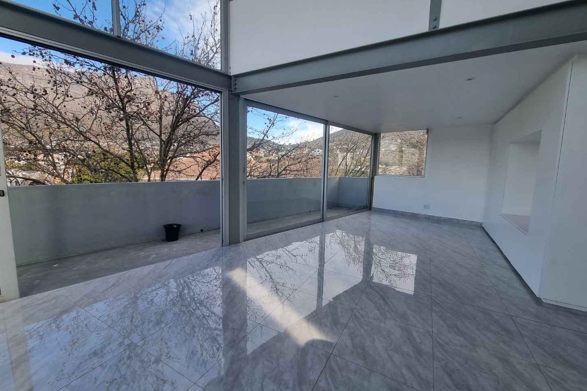 Spacious, modern open-plan living area featuring polished porcelain tiles, exposed steel structural elements, and expansive floor-to-ceiling glass doors opening onto a private balcony.