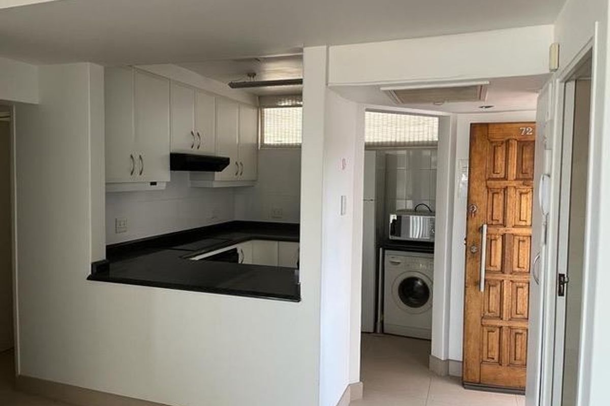 Compact kitchen area featuring built-in cabinetry, dark countertops, and an adjacent laundry nook with a solid wood entrance door.