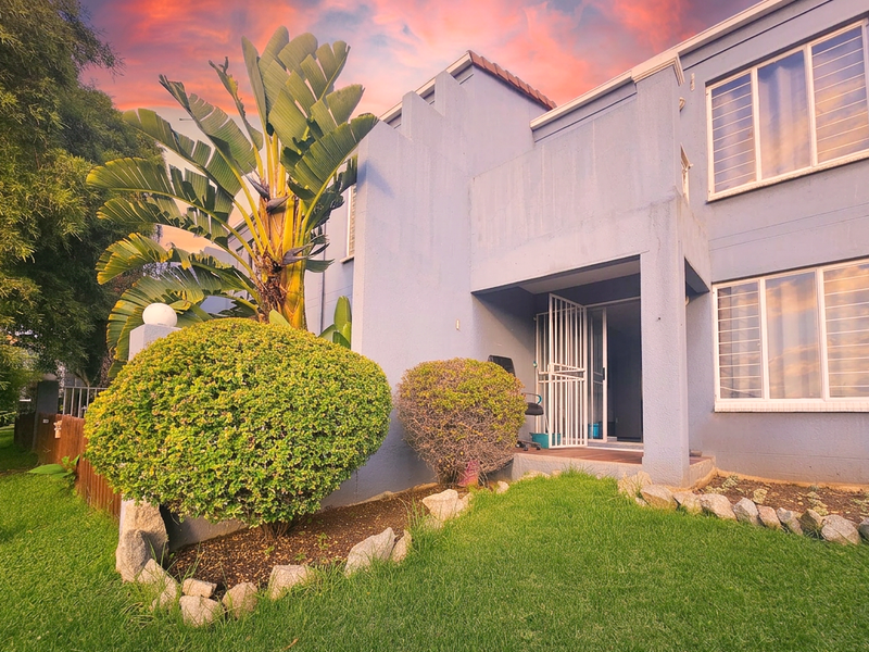 Front elevation of an apartment unit featuring a small entrance porch, security gates, and established garden landscaping.