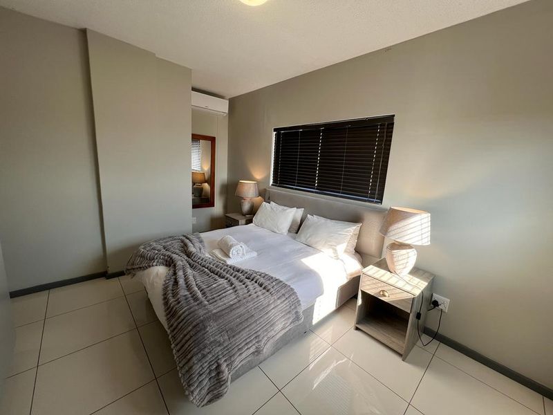 A well-maintained bedroom featuring neutral wall tones, tiled flooring, an integrated air conditioning unit, and venetian blinds for privacy.