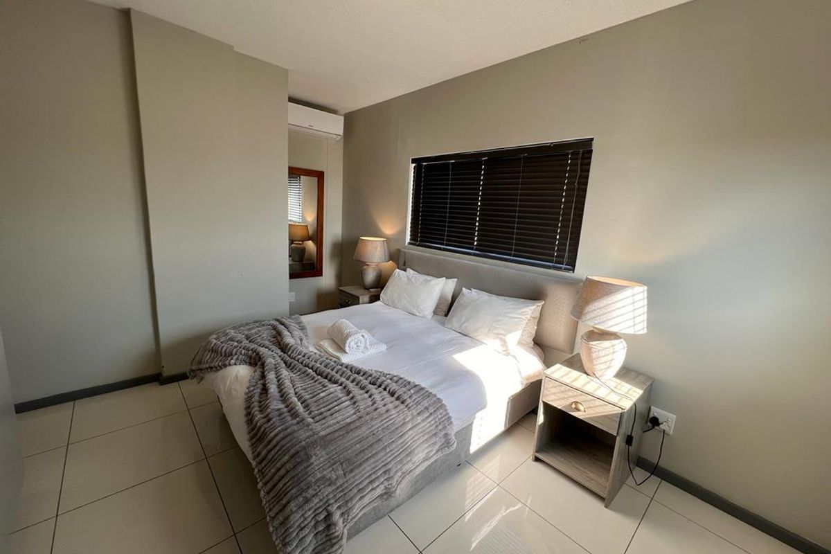A well-maintained bedroom featuring neutral wall tones, tiled flooring, an integrated air conditioning unit, and venetian blinds for privacy.