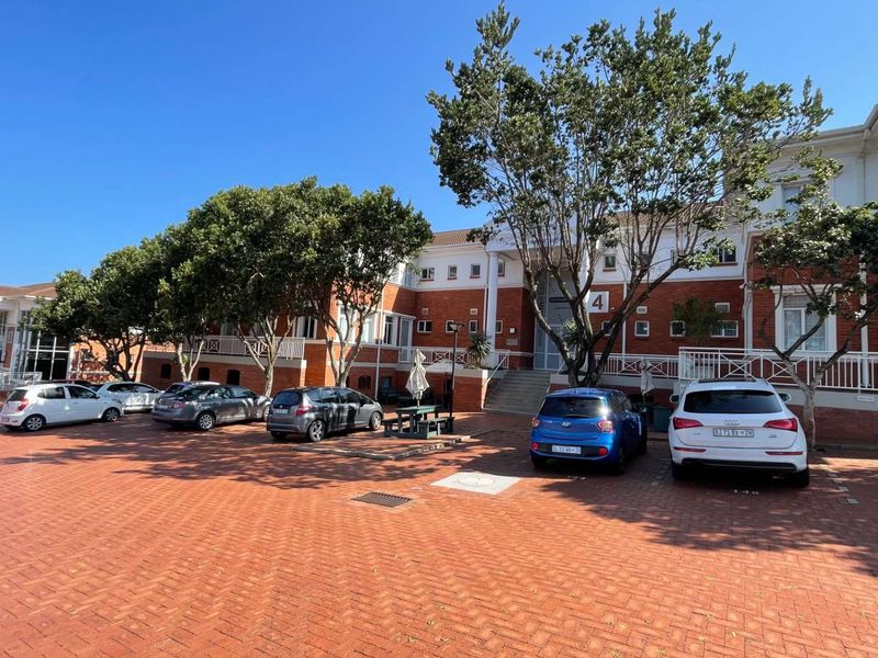 Exterior view of a multi-story office building featuring a red brick facade, white architectural detailing, and a large paved parking area.