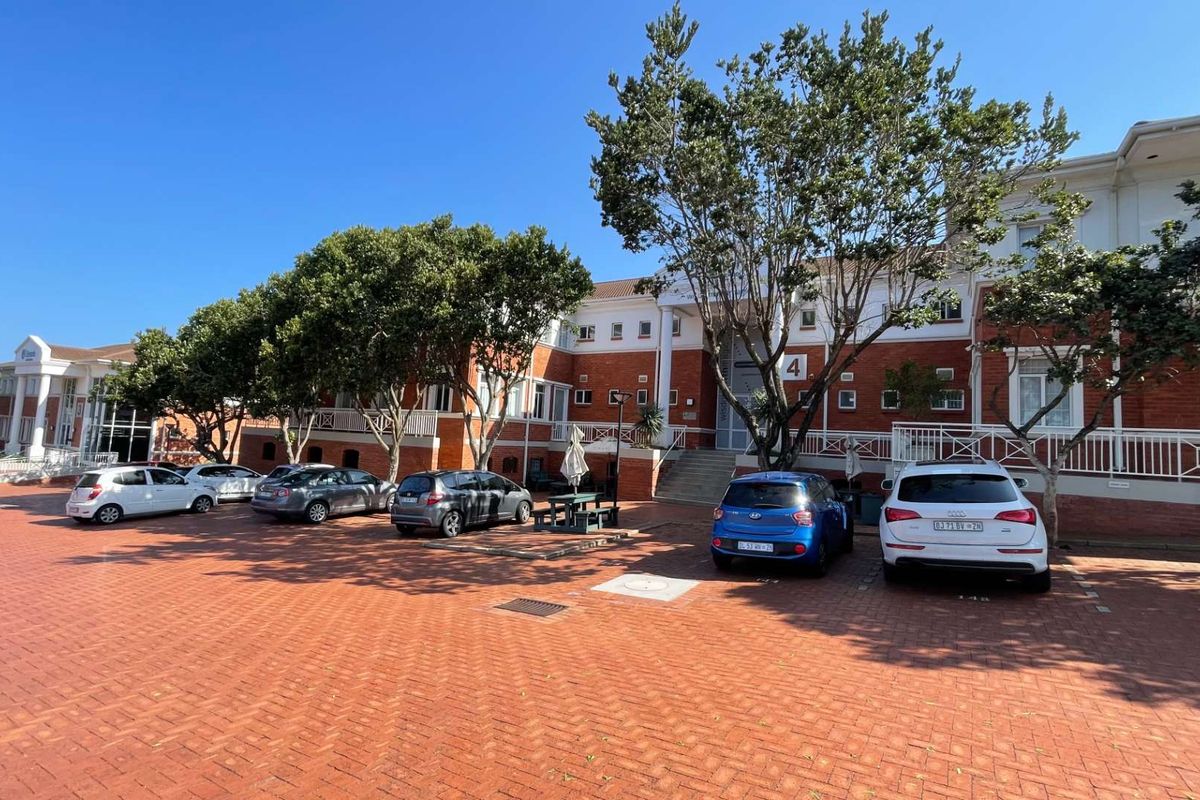 Exterior view of a multi-story office building featuring a red brick facade, white architectural detailing, and a large paved parking area.