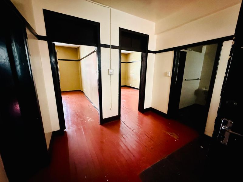 An empty hallway featuring original timber flooring and dark-painted door frames, providing access to multiple rooms within the apartment.