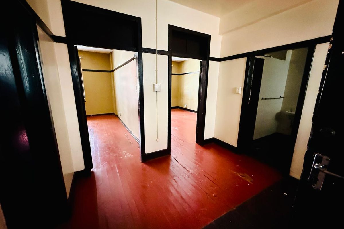 An empty hallway featuring original timber flooring and dark-painted door frames, providing access to multiple rooms within the apartment.