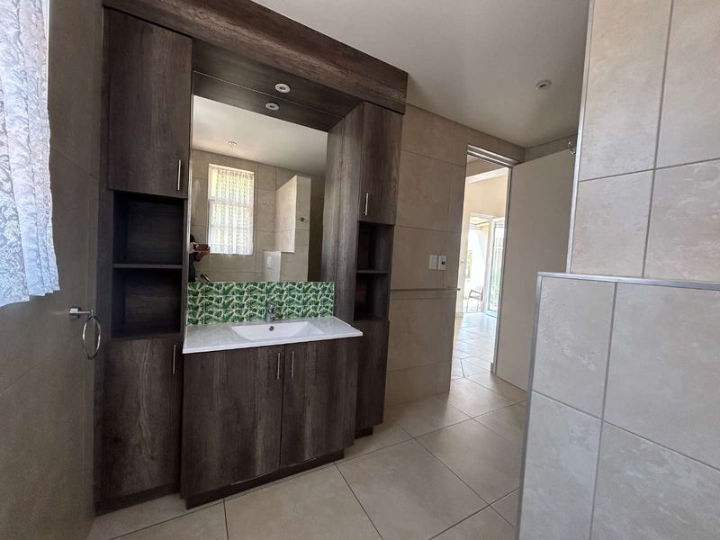 A modern bathroom featuring a dark wood built-in vanity with an integrated mirror, decorative backsplash tiling, and neutral floor tiles.