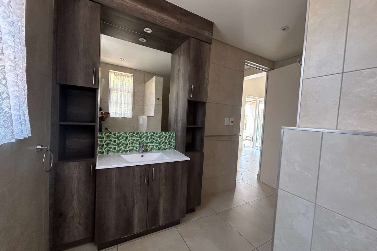 A modern bathroom featuring a dark wood built-in vanity with an integrated mirror, decorative backsplash tiling, and neutral floor tiles.