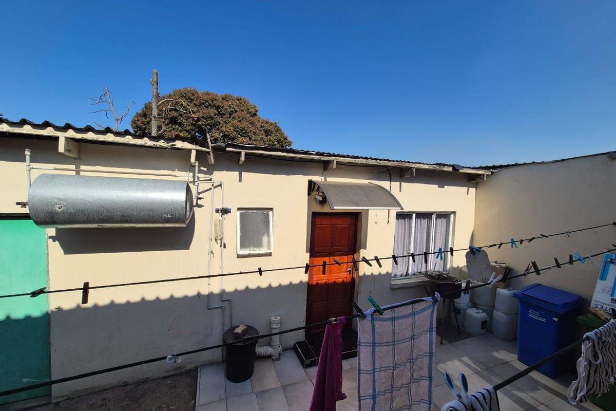 Rear exterior view of the property featuring a tiled patio area, external geyser, and access door with a protective awning.