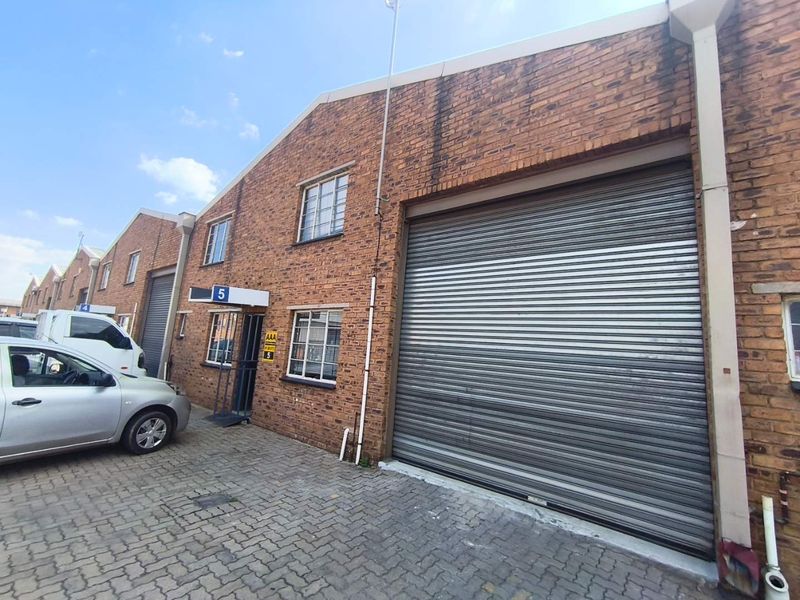 Industrial unit exterior featuring a large roller shutter door, brick facade, and paved driveway access.