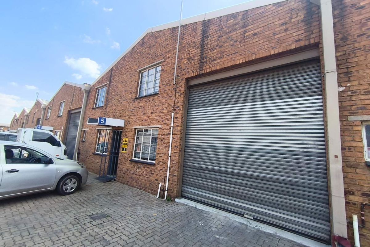Industrial unit exterior featuring a large roller shutter door, brick facade, and paved driveway access.