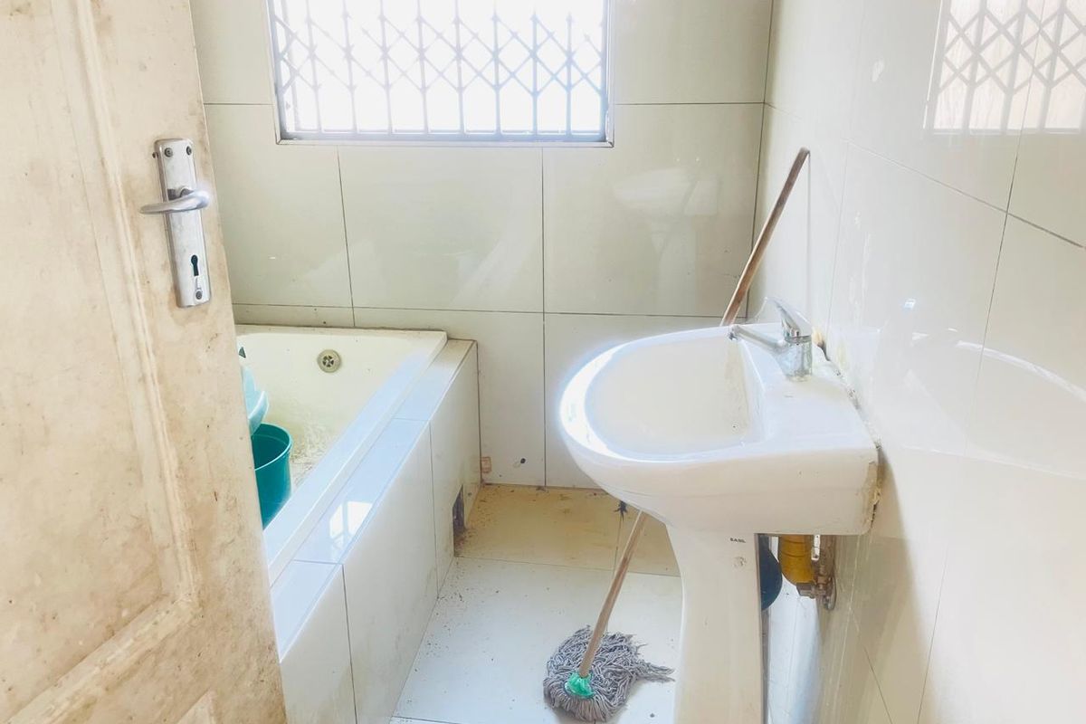 A compact bathroom featuring a built-in bathtub, pedestal basin, and tiled walls, requiring maintenance and cosmetic updates.