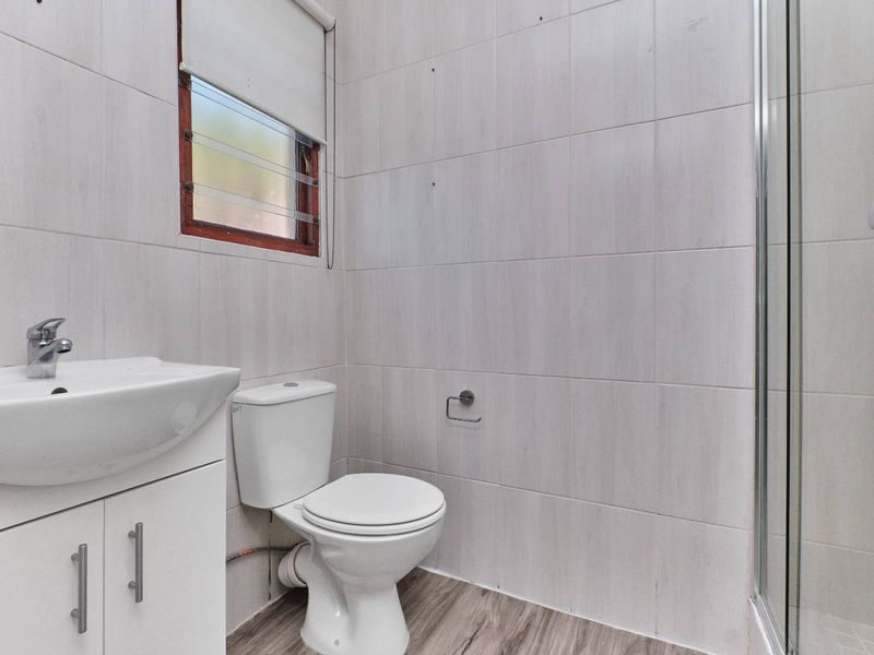 A functional bathroom featuring a vanity basin, toilet, and shower enclosure with neutral wall tiling and wood-look flooring.
