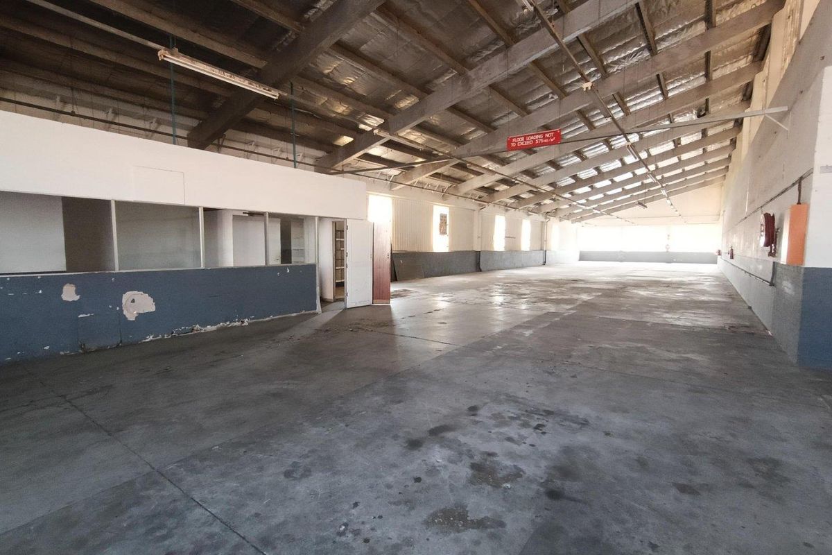 Spacious industrial warehouse area featuring exposed steel roof trusses, concrete flooring, and a partitioned office section, suitable for various commercial or storage uses.