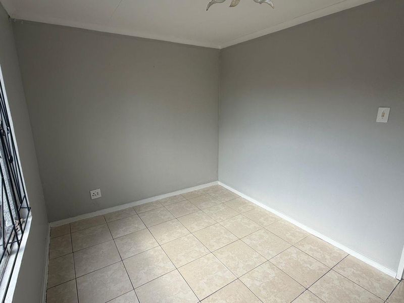 A vacant bedroom featuring neutral grey walls, tiled flooring, and a window fitted with a security gate.
