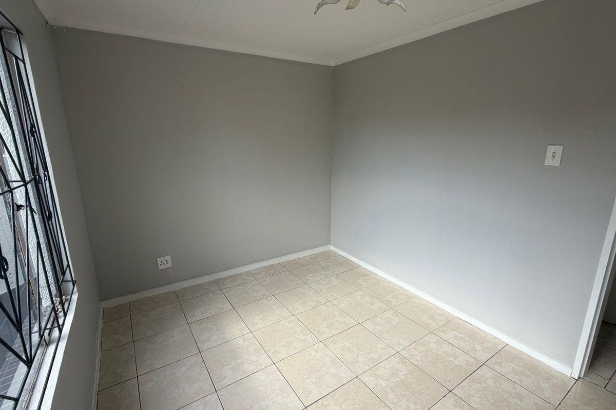 A vacant bedroom featuring neutral grey walls, tiled flooring, and a window fitted with a security gate.