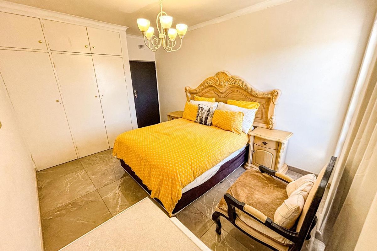 A bedroom featuring built-in cupboards, tiled flooring, and a central chandelier, offering a functional space with potential for modern updates.