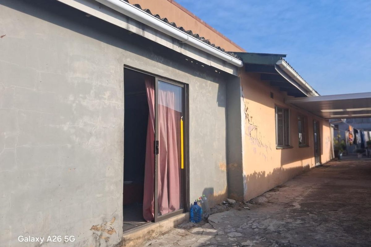 Rear exterior view of the property showing a sliding door entrance, concrete patio area, and visible wear to the exterior wall plaster and paintwork.