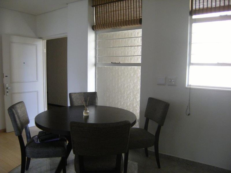 A dining area featuring tiled flooring, louvered windows with bamboo blinds, and access to an adjacent hallway.