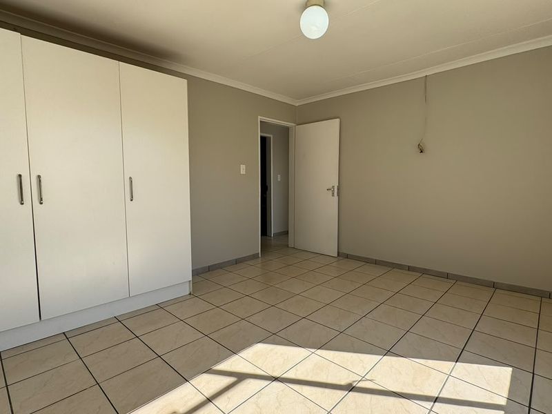 A clean, empty bedroom featuring neutral tiled flooring, built-in cupboards, and a simple ceiling light fixture.