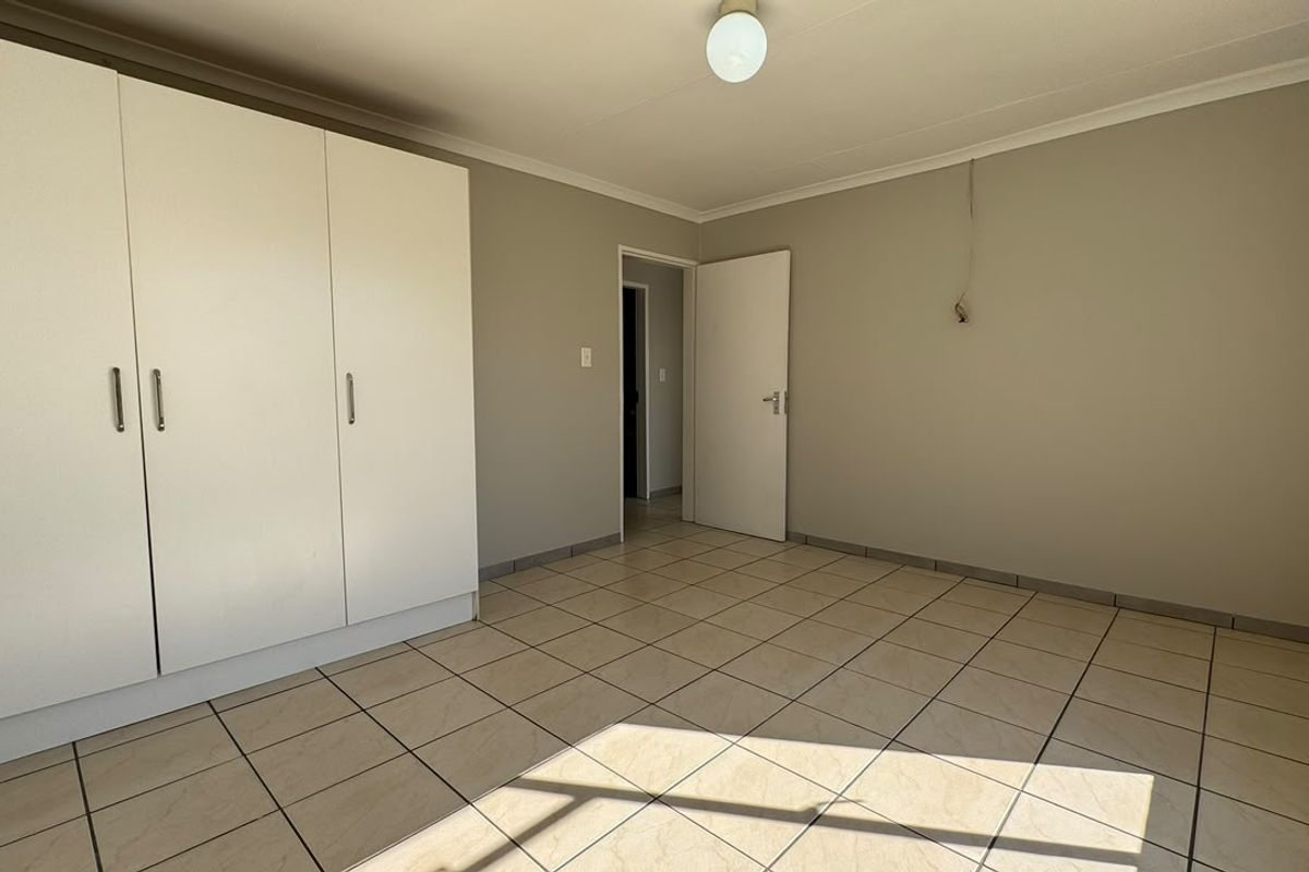 A clean, empty bedroom featuring neutral tiled flooring, built-in cupboards, and a simple ceiling light fixture.